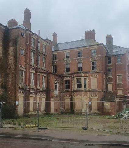 A derelict red brick building boarded up behind fencing